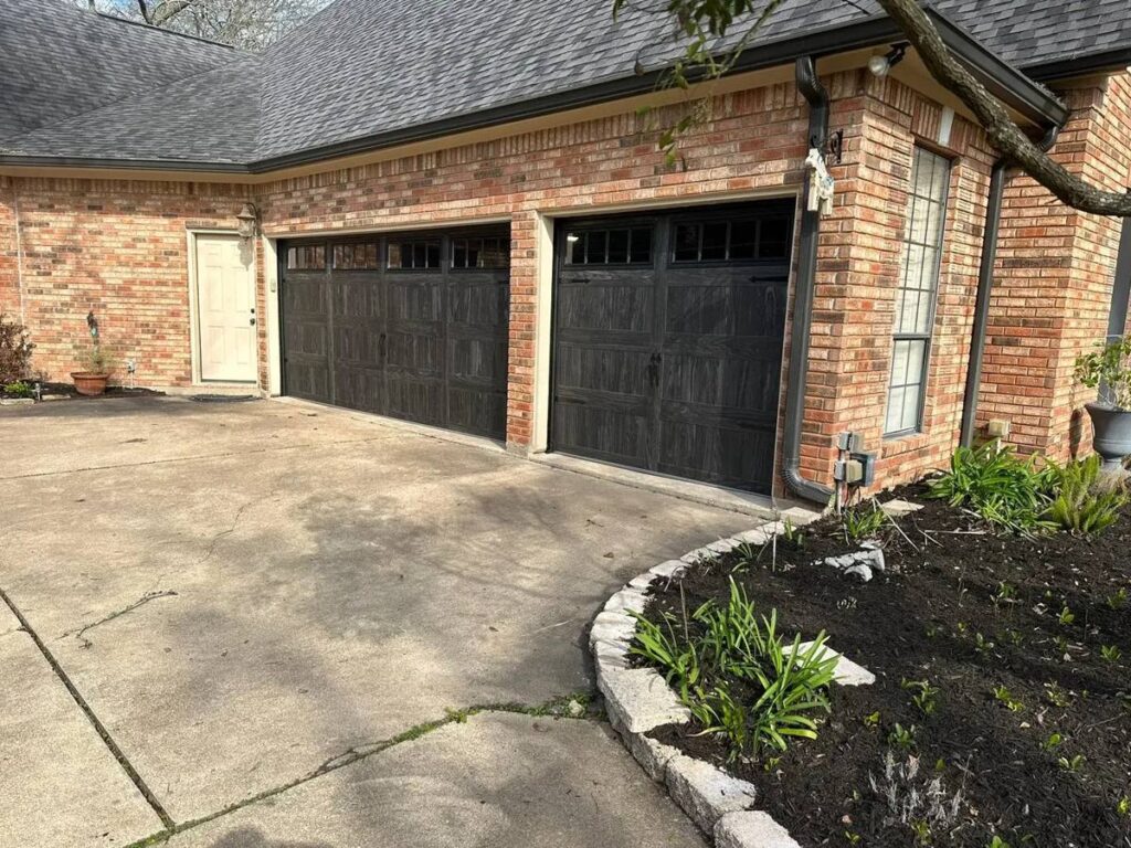 Two black carriage-style garage doors on a brick home